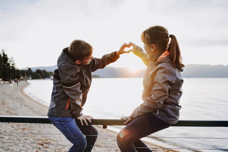 Kids sitting on rail making heart shape with their hands as sun sets at Lake Tahoe