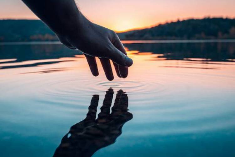 Hand touching and reflecting off lake water